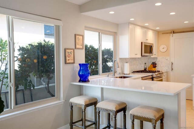 kitchen featuring a breakfast bar, sink, appliances with stainless steel finishes, kitchen peninsula, and white cabinets