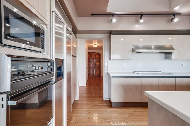 kitchen featuring black oven, light hardwood / wood-style flooring, rail lighting, electric cooktop, and built in fridge