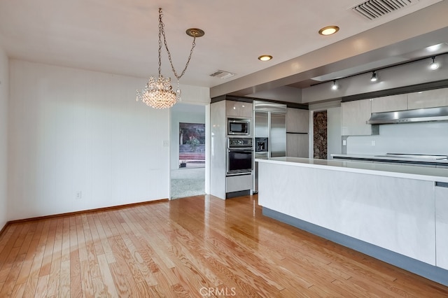 kitchen featuring rail lighting, built in appliances, decorative light fixtures, light hardwood / wood-style floors, and white cabinets