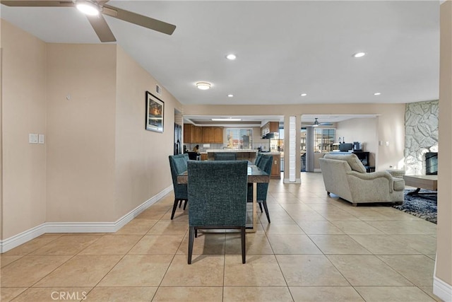 dining room featuring ceiling fan, a fireplace, and light tile patterned floors