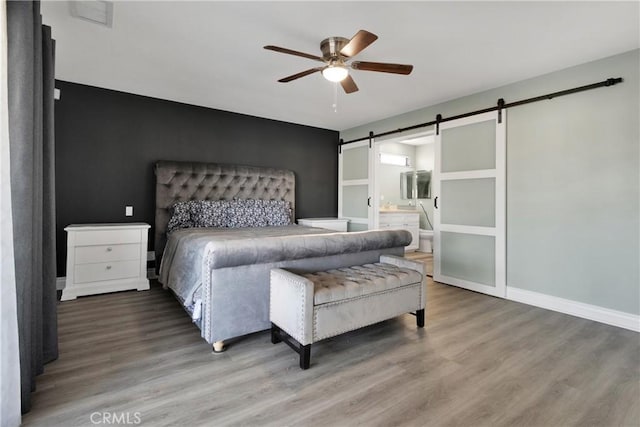 bedroom with hardwood / wood-style floors, ensuite bath, a barn door, and ceiling fan