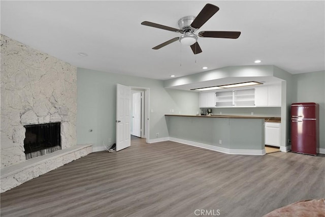 unfurnished living room featuring hardwood / wood-style floors, a stone fireplace, and ceiling fan