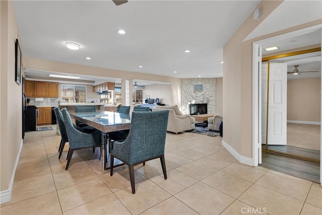 dining room with ceiling fan, a stone fireplace, and light tile patterned floors