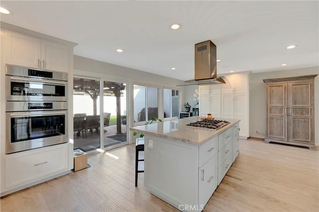 kitchen featuring appliances with stainless steel finishes, white cabinetry, a center island, island range hood, and light stone countertops