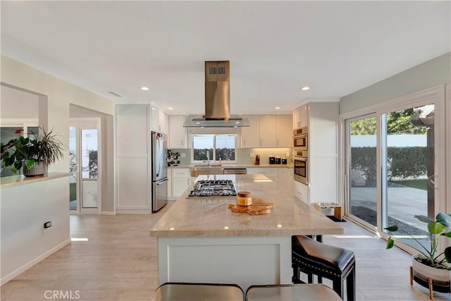 kitchen with light hardwood / wood-style flooring, appliances with stainless steel finishes, island exhaust hood, light stone countertops, and white cabinets