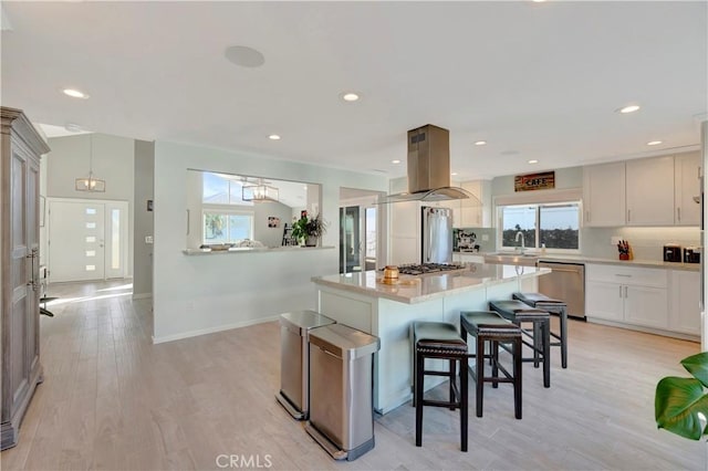 kitchen with appliances with stainless steel finishes, island range hood, white cabinets, a center island, and plenty of natural light