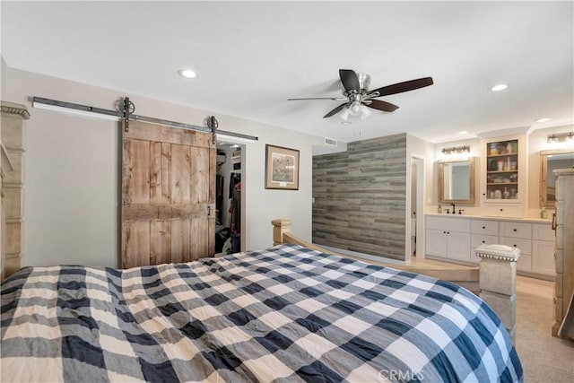 bedroom featuring connected bathroom, a barn door, a walk in closet, light colored carpet, and a closet