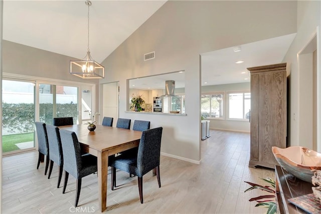 dining space featuring a chandelier, high vaulted ceiling, and light hardwood / wood-style flooring