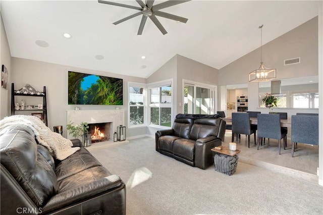 living room featuring ceiling fan with notable chandelier, high vaulted ceiling, light colored carpet, and a fireplace