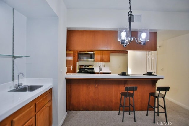 kitchen with appliances with stainless steel finishes, decorative light fixtures, sink, a kitchen breakfast bar, and light carpet