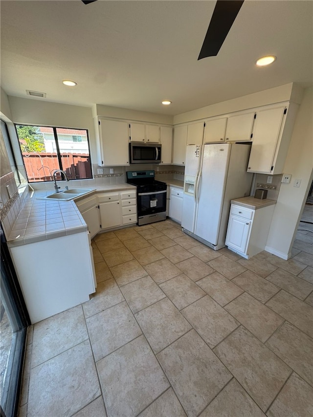 kitchen featuring stainless steel appliances, tile countertops, sink, and white cabinets