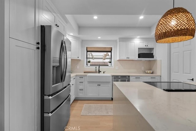 kitchen featuring pendant lighting, sink, white cabinets, stainless steel appliances, and light wood-type flooring