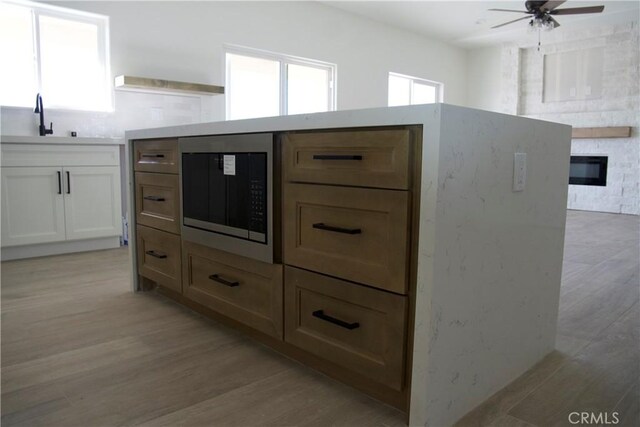 room details with stainless steel microwave, a large fireplace, sink, white cabinets, and light hardwood / wood-style floors