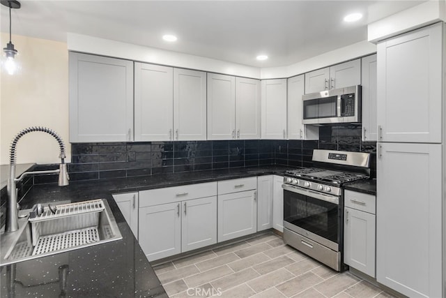 kitchen with pendant lighting, sink, dark stone countertops, backsplash, and stainless steel appliances