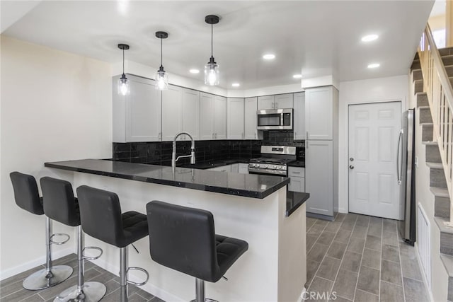 kitchen featuring appliances with stainless steel finishes, a kitchen bar, kitchen peninsula, and hanging light fixtures