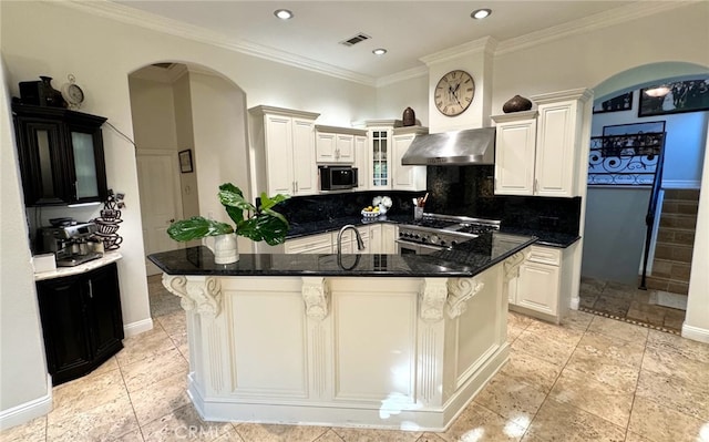 kitchen with a kitchen breakfast bar, decorative backsplash, dark stone counters, wall chimney range hood, and a spacious island