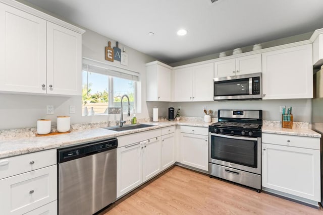 kitchen with sink, light hardwood / wood-style flooring, stainless steel appliances, light stone countertops, and white cabinets