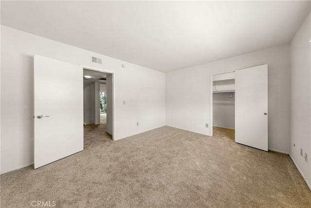 unfurnished bedroom with a walk in closet, light carpet, and a closet