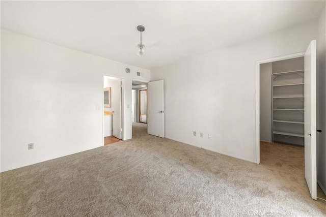 unfurnished bedroom with a walk in closet, a closet, and light carpet