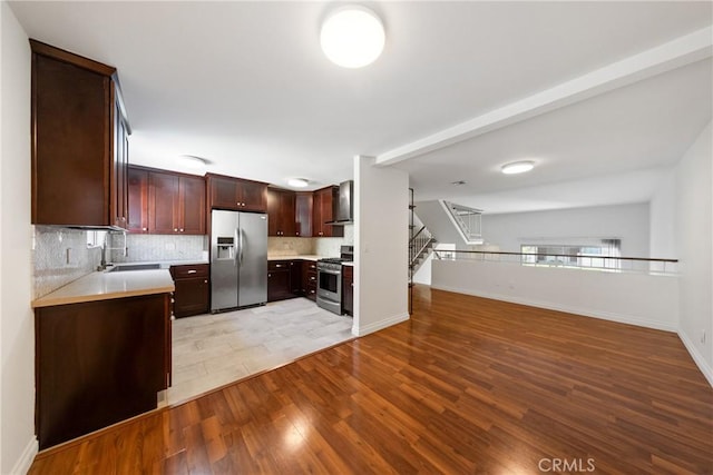 kitchen with tasteful backsplash, sink, stainless steel appliances, light wood-type flooring, and wall chimney exhaust hood