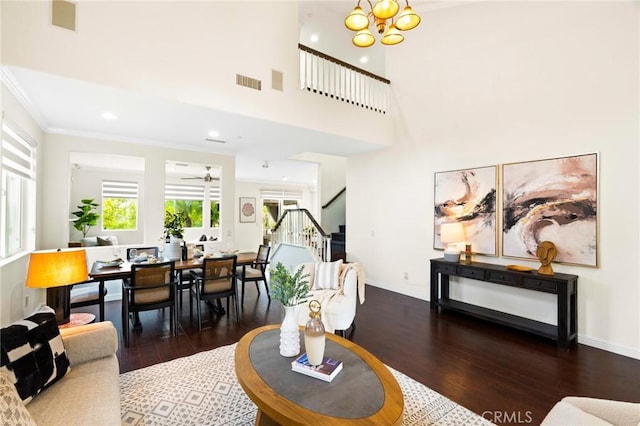 living room with dark hardwood / wood-style flooring, crown molding, ceiling fan with notable chandelier, and a high ceiling