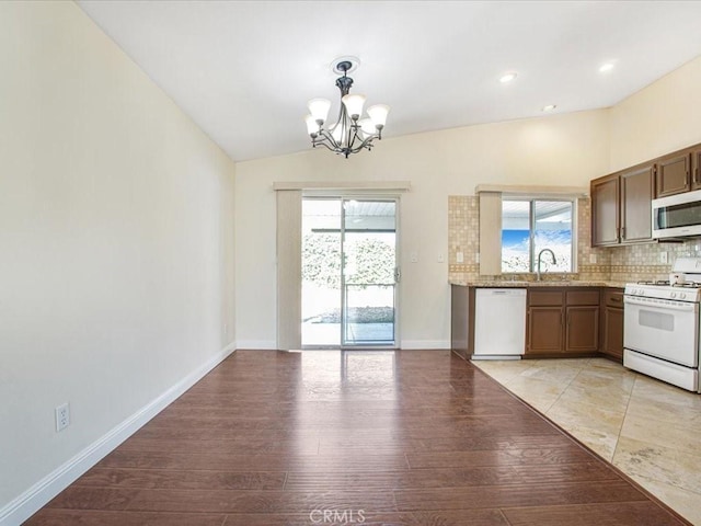 kitchen featuring light wood finished floors, lofted ceiling, decorative backsplash, a chandelier, and white appliances