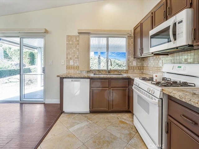 kitchen with light stone counters, light tile patterned floors, tasteful backsplash, a sink, and white appliances