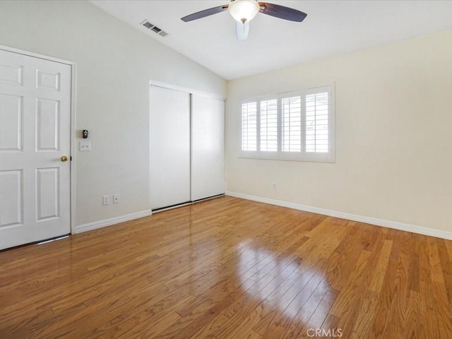 unfurnished bedroom featuring wood finished floors, visible vents, baseboards, vaulted ceiling, and a closet