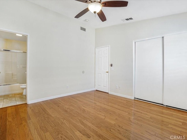 unfurnished bedroom featuring baseboards, wood finished floors, visible vents, and connected bathroom