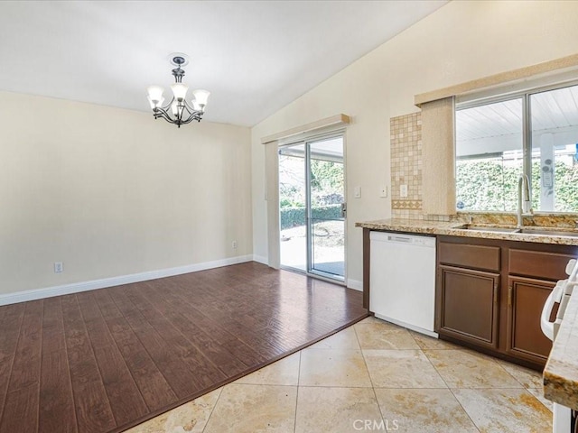 kitchen featuring light stone counters, white dishwasher, a notable chandelier, a sink, and vaulted ceiling