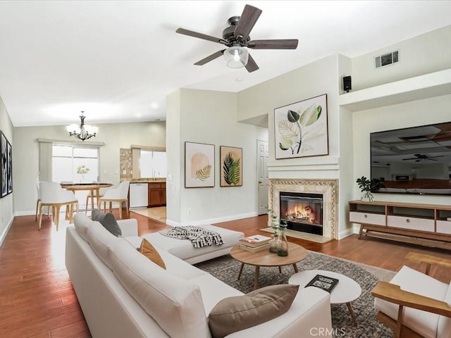 living area featuring visible vents, ceiling fan with notable chandelier, lofted ceiling, and wood finished floors