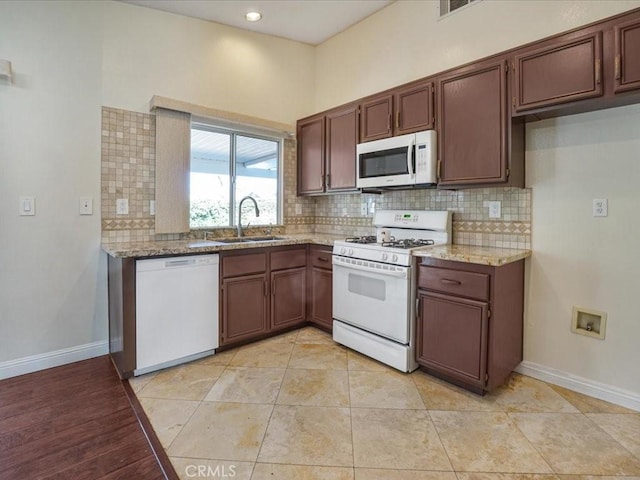 kitchen featuring white appliances, a sink, baseboards, light stone countertops, and tasteful backsplash