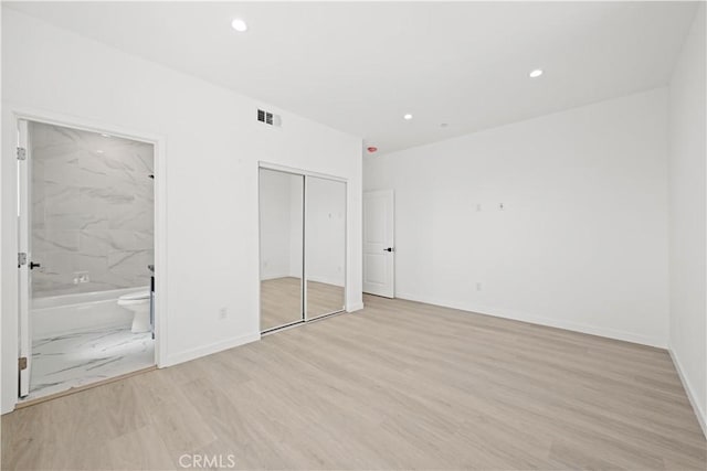 unfurnished bedroom featuring a closet, ensuite bathroom, and light hardwood / wood-style flooring