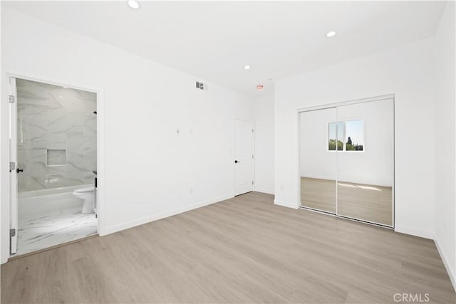 unfurnished bedroom featuring light hardwood / wood-style flooring, a closet, and ensuite bathroom