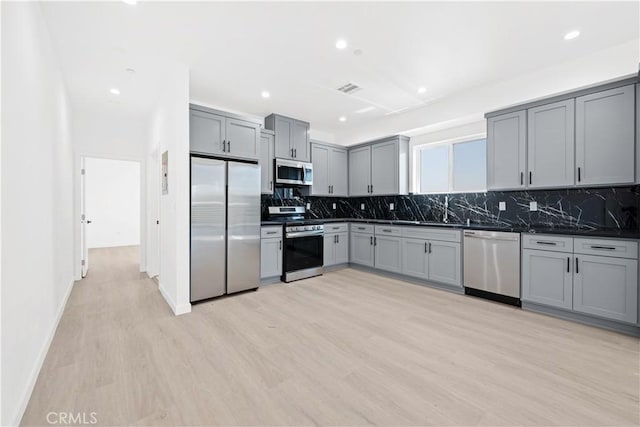 kitchen with backsplash, stainless steel appliances, light hardwood / wood-style floors, and gray cabinetry