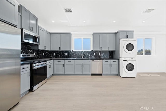 kitchen featuring stacked washer / dryer, a wealth of natural light, appliances with stainless steel finishes, and gray cabinetry