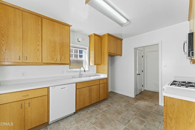 kitchen featuring brown cabinets, light countertops, stainless steel microwave, white dishwasher, and a sink