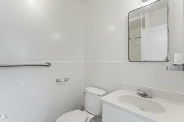 bathroom with toilet, a wainscoted wall, tile walls, and vanity