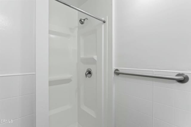 bathroom with a shower stall, tile walls, and wainscoting