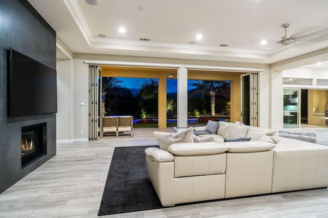 living room with a raised ceiling, ornamental molding, a large fireplace, and light wood-type flooring