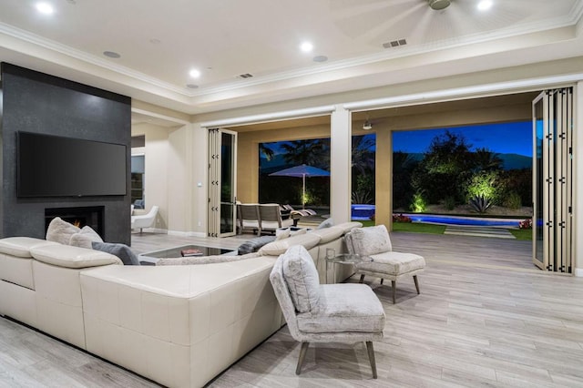 living room with a raised ceiling, crown molding, and light hardwood / wood-style flooring