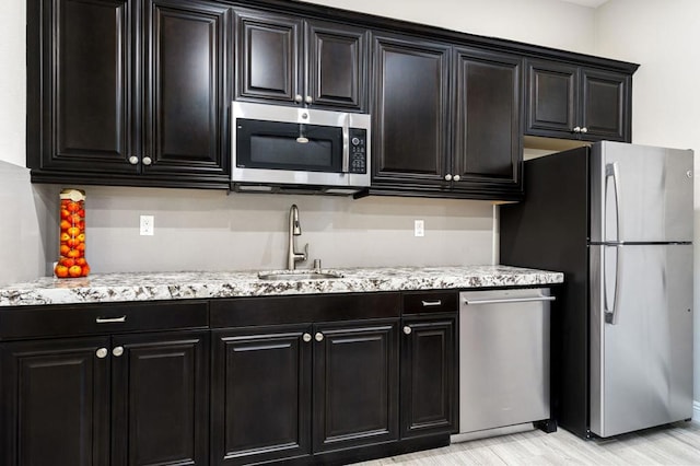 kitchen featuring sink, light hardwood / wood-style flooring, light stone countertops, and appliances with stainless steel finishes