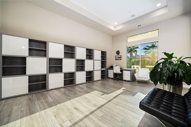 living area featuring a towering ceiling, a tray ceiling, and light hardwood / wood-style floors