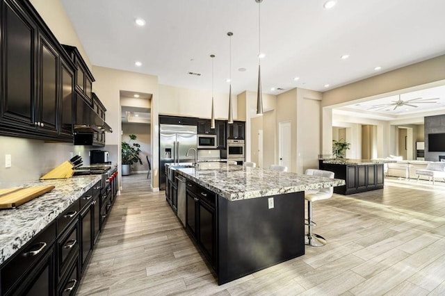 kitchen featuring premium appliances, a kitchen breakfast bar, hanging light fixtures, and a large island with sink