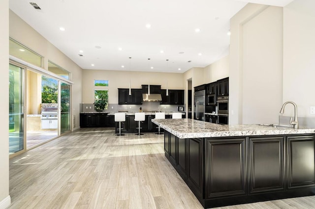 kitchen with sink, a center island, stainless steel appliances, light stone countertops, and light wood-type flooring