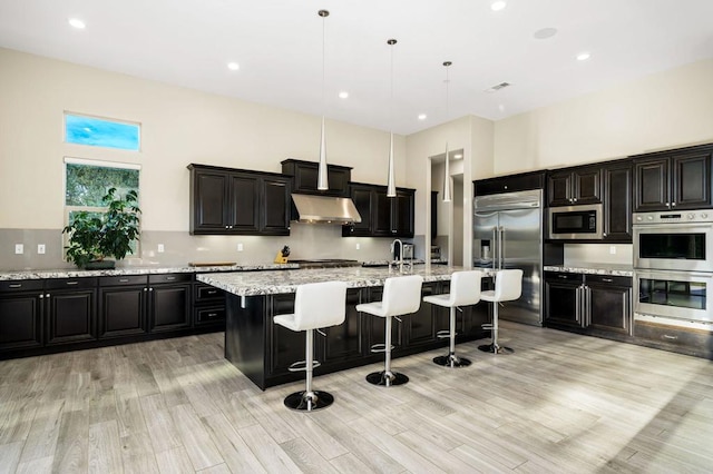 kitchen with built in appliances, a kitchen breakfast bar, an island with sink, pendant lighting, and a high ceiling