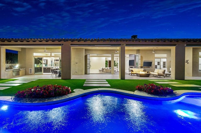 back house at night with ceiling fan, a yard, a patio, an outdoor hangout area, and an outdoor kitchen