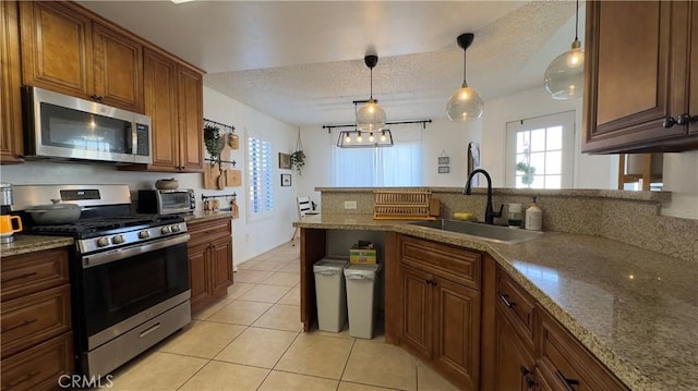 kitchen featuring stainless steel appliances, light stone countertops, sink, and decorative light fixtures