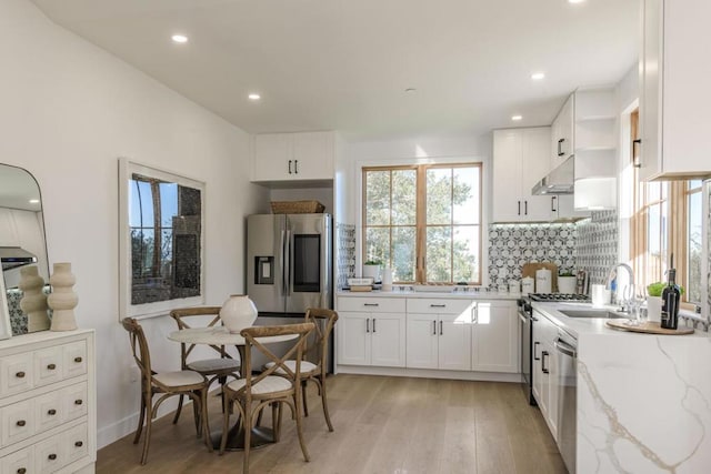 kitchen with sink, stainless steel appliances, light stone countertops, white cabinets, and decorative backsplash