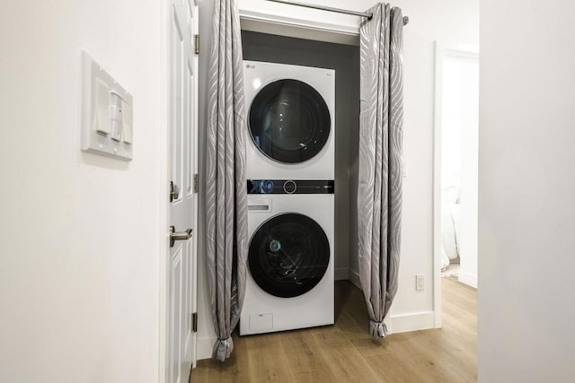 clothes washing area with stacked washer and clothes dryer and light wood-type flooring